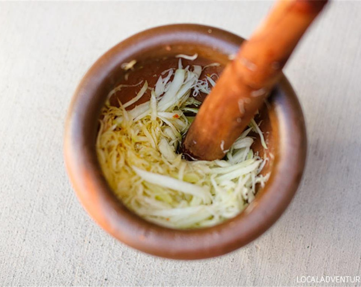 step 3 Put a handful of shredded vegetable and fruit into the mortar and pestle and mix. Then mash together the remainder of the papaya and Cherry Tomatoes (10). Add the Fish Sauce (1 Tbsp), Lime (1), Granulated Sugar (1 tsp), and mash together.