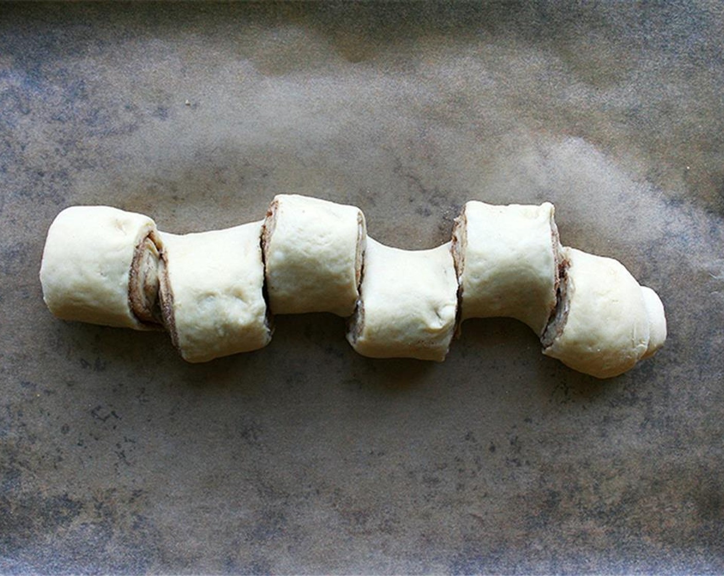 step 8 Roll into a log starting with the short side. Place each log seam side down on a baking sheet lined with parchment paper. Make cuts every couple inches straight down leaving the last layer intact. Gently pull the sections outward. Let rise for about 40 to 45 minutes or until slightly puffed.