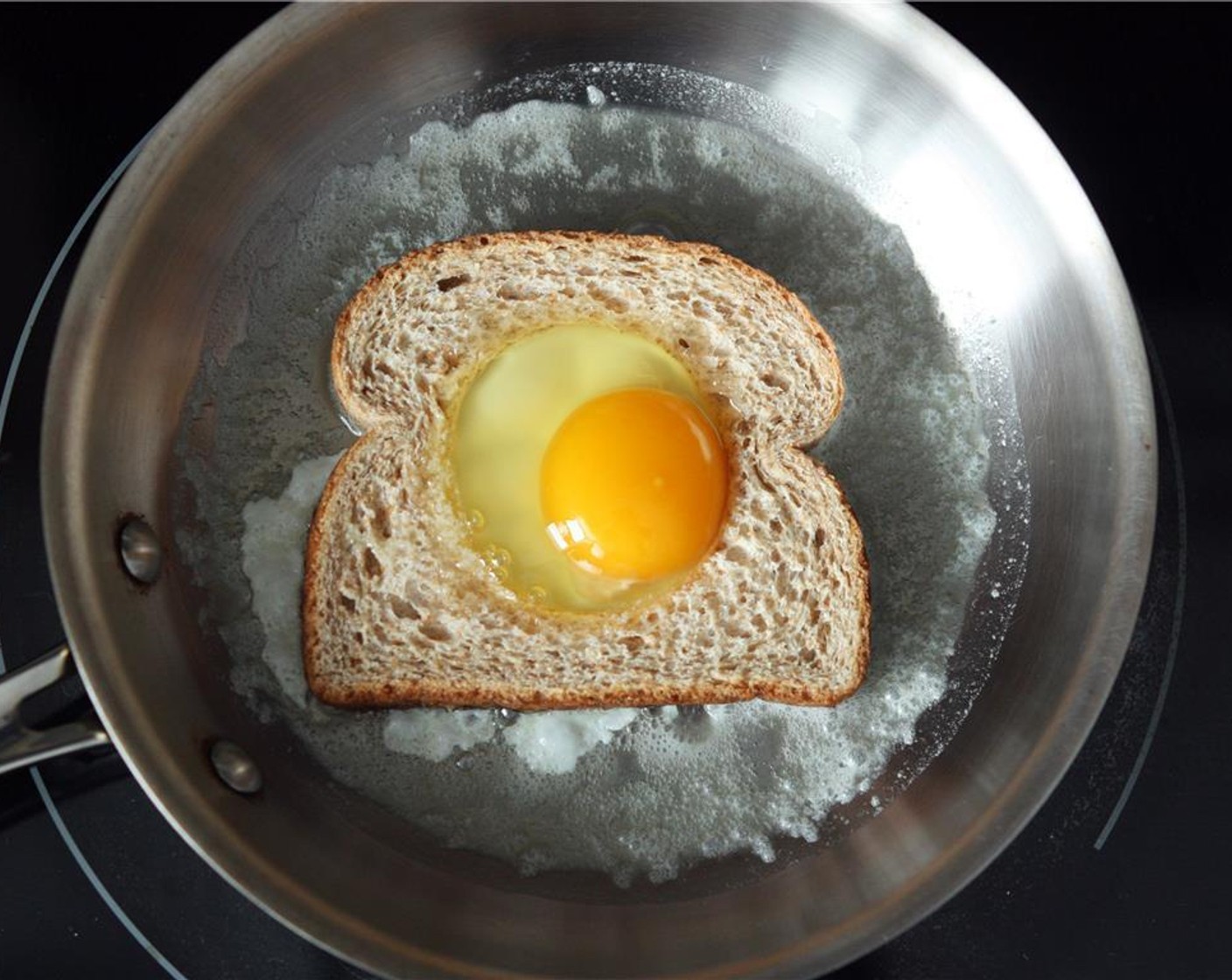 step 3 Once butter has fully melted and has begun to bubble slightly, place the bread into the skillet and the center piece to the side. Carefully crack the Egg (1) into the hole in the bread.