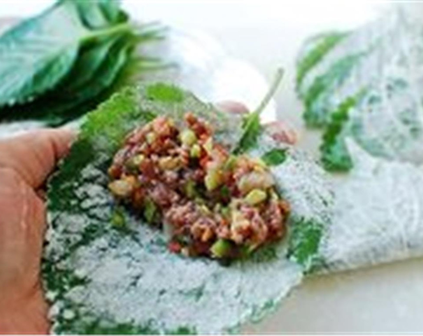 step 6 Place a perilla leaf on your hand. Add about a tablespoon of stuffing to the upper half of the perilla leaf. Spread evenly with a spoon. Bring the other half of the leaf over to cover the stuffing. Lightly flatten it with your hand.