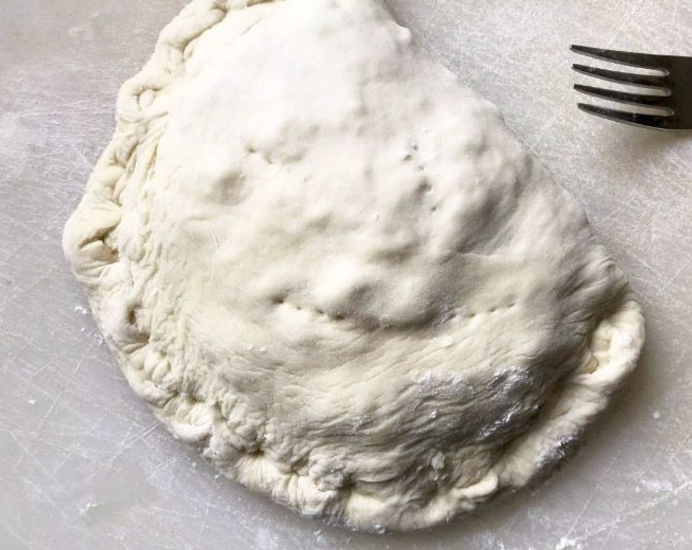 step 5 Fold a short end of each dough oval over its filling, forming 2 half-moon shaped calzones. Roll the bottom edge up and over, twisting and pressing with your thumb to seal as you go. The decorative rolled edge will be substantial so that it doesn't become overly browned during the baking process. Prick the top of each calzone in a few places with a fork to vent.