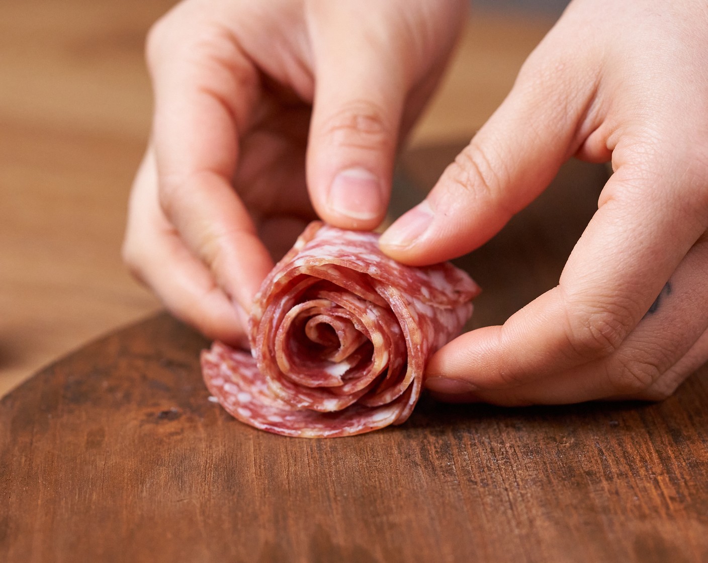 step 2 Make the salami rose by layering 5-6 pieces of Salami (1/2 cup) on the surface, and make sure 1/3 or 1/2 of each piece is overlapping with another piece. Fold the salami pieces in half and roll them up from left to right, making a flower shape. Set aside.