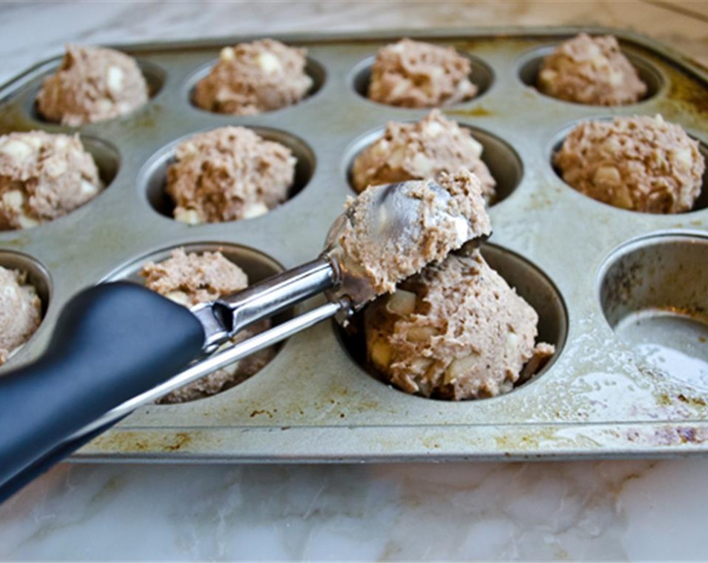 step 7 Use an ice-cream scooper or large spoon to divide the batter evenly among the prepared muffin cups. The cups should be full. Sprinkle the Dark Brown Sugar (2 Tbsp) evenly over top.