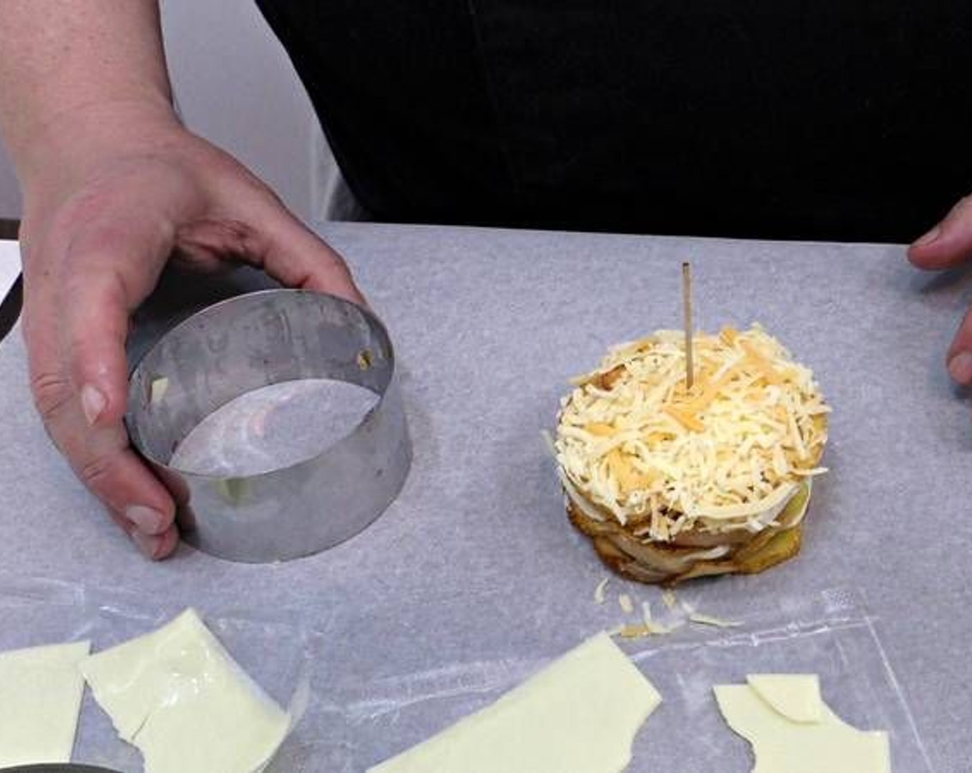 step 6 Layer potato slices, Serrano ham, and Processed Cheese (7 slices) on a baking tray lined with baking paper using a ring mold and a skewer to hold it together. Make sure your first and last layers are potato slices. At the very top add a bit of Shredded Cheese (1 cup) and remove the ring mold.