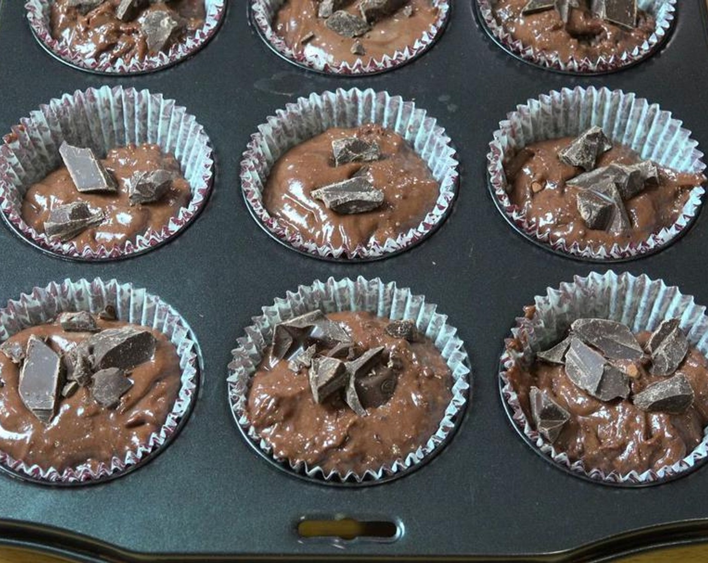 step 4 Divide the batter between the holes of a 12-hole muffin tin lined with paper cases. Sprinkle Semi-Sweet Dark Chocolate (1/2 cup) over the top of each muffin and press down lightly.