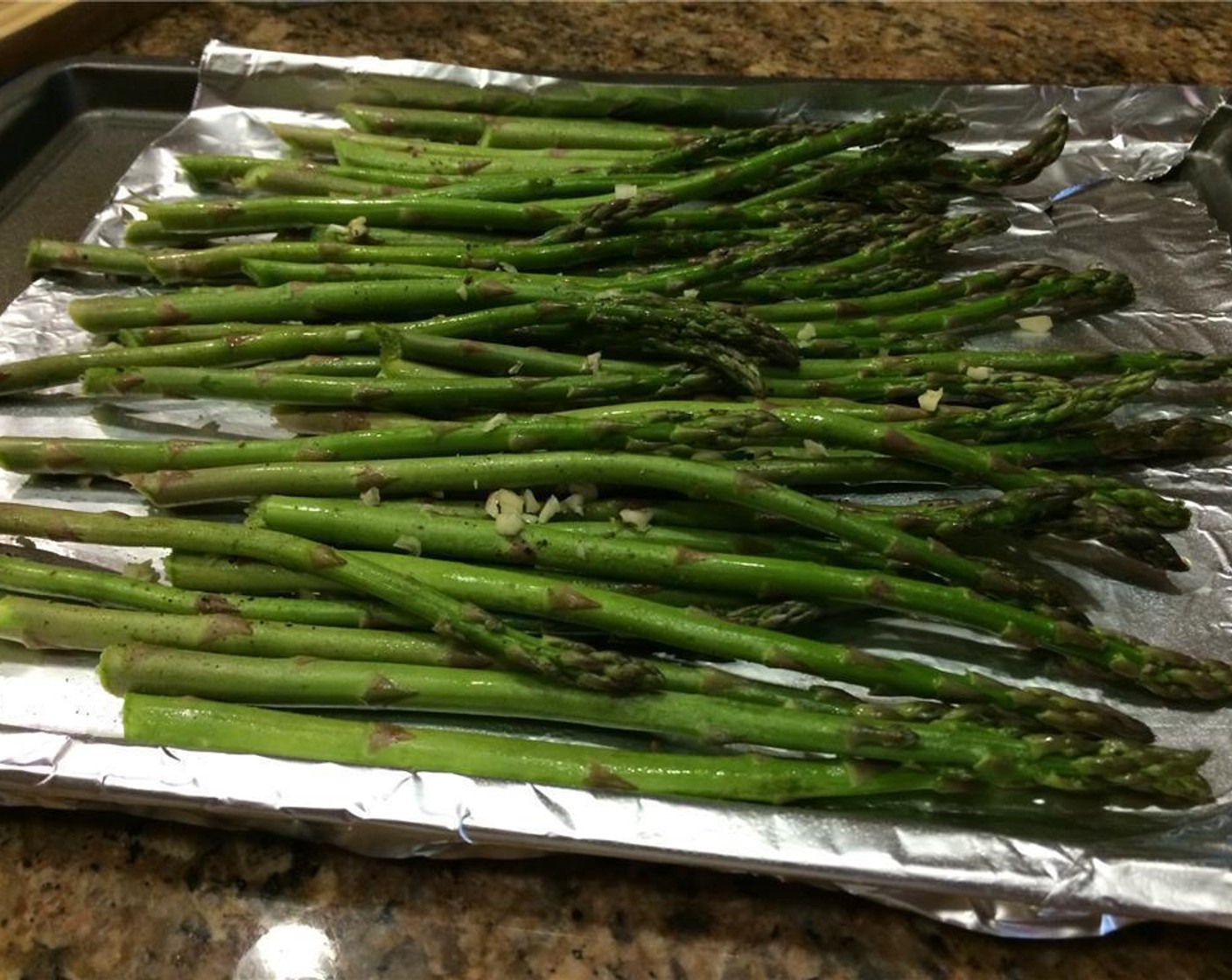 step 2 Place the Asparagus (1 bunch) on the pan and spread out evenly. Add Garlic (1 clove) and season with Salt (to taste) and Ground Black Pepper (to taste). Bake for 12 minutes or until tender.