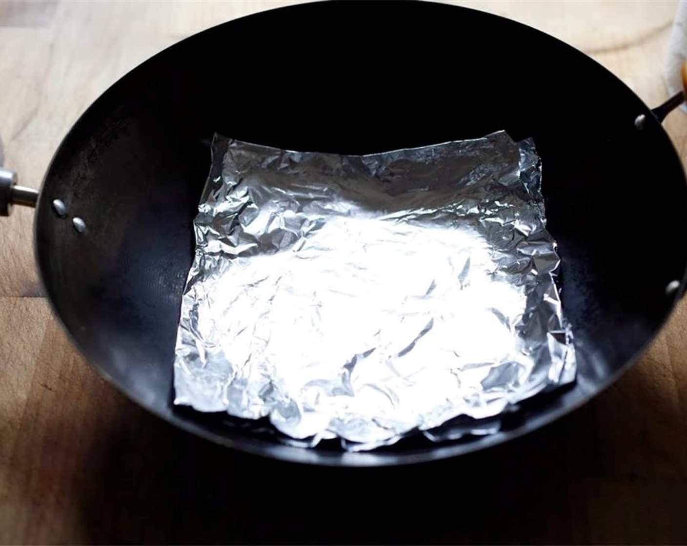 step 8 Take a large piece of foil and fold in half, then in half again so you have an 8 inch square, four layers thick. Place foil in the bottom of the wok.