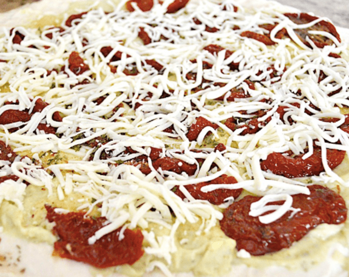 step 9 Spread the pesto béchamel in an even layer on the dough, leaving a 1 inch border to have a crust to grab. Lay out Sun-Dried Tomatoes (1 can) evenly on the sauce, then season it all with the Simply Organic Garlic Powder (1/2 tsp) and Dried Parsley (1/2 tsp), add Shredded Mozzarella Cheese (1 1/3 cups) and garnish with Baby Arugula (1 cup).