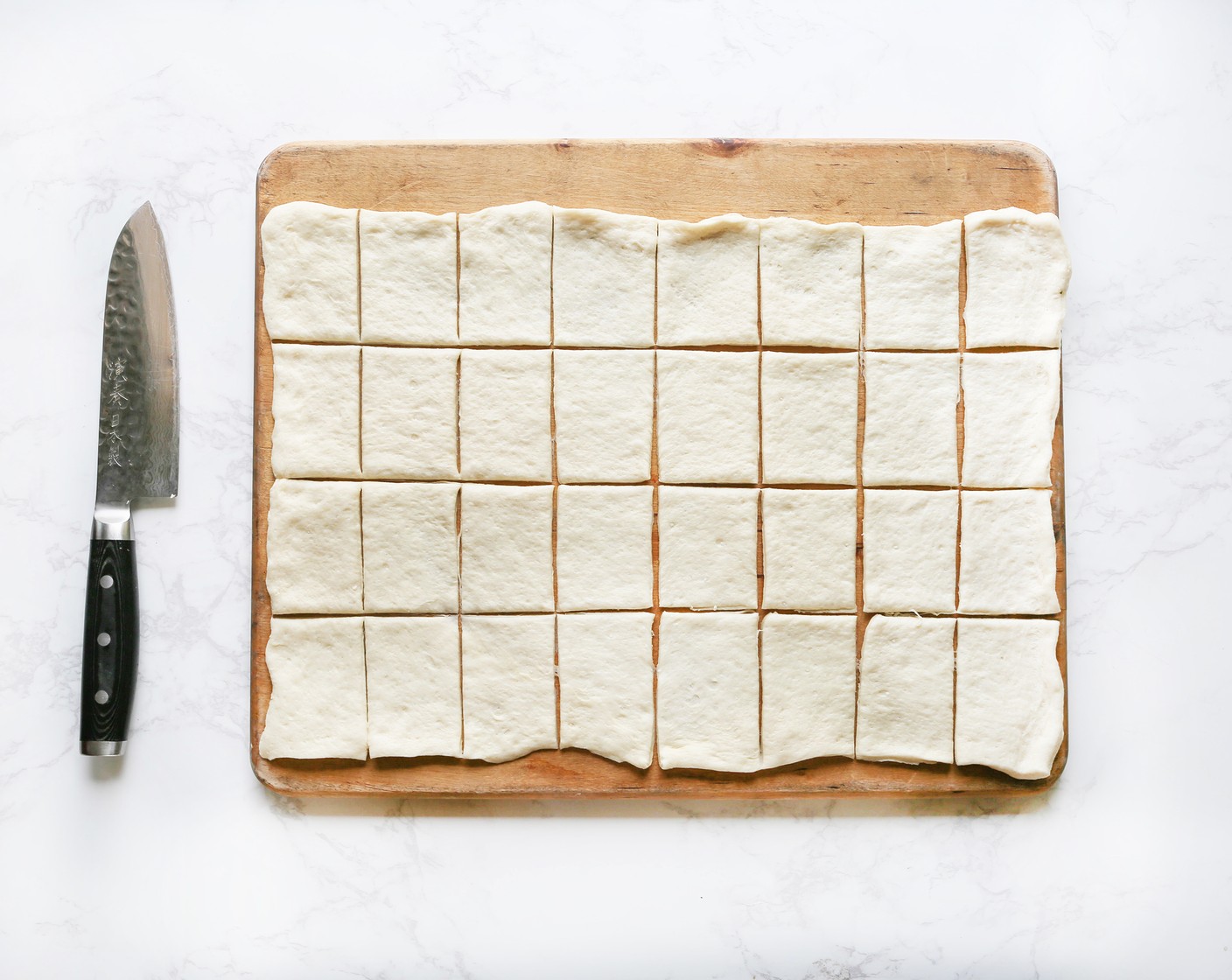 step 3 Unroll the Pizza Dough (1 can) and place on a flat surface. Using either a sharp knife or pizza cutter, cut dough rectangle into 4 rows lengthwise and 8 rows across.