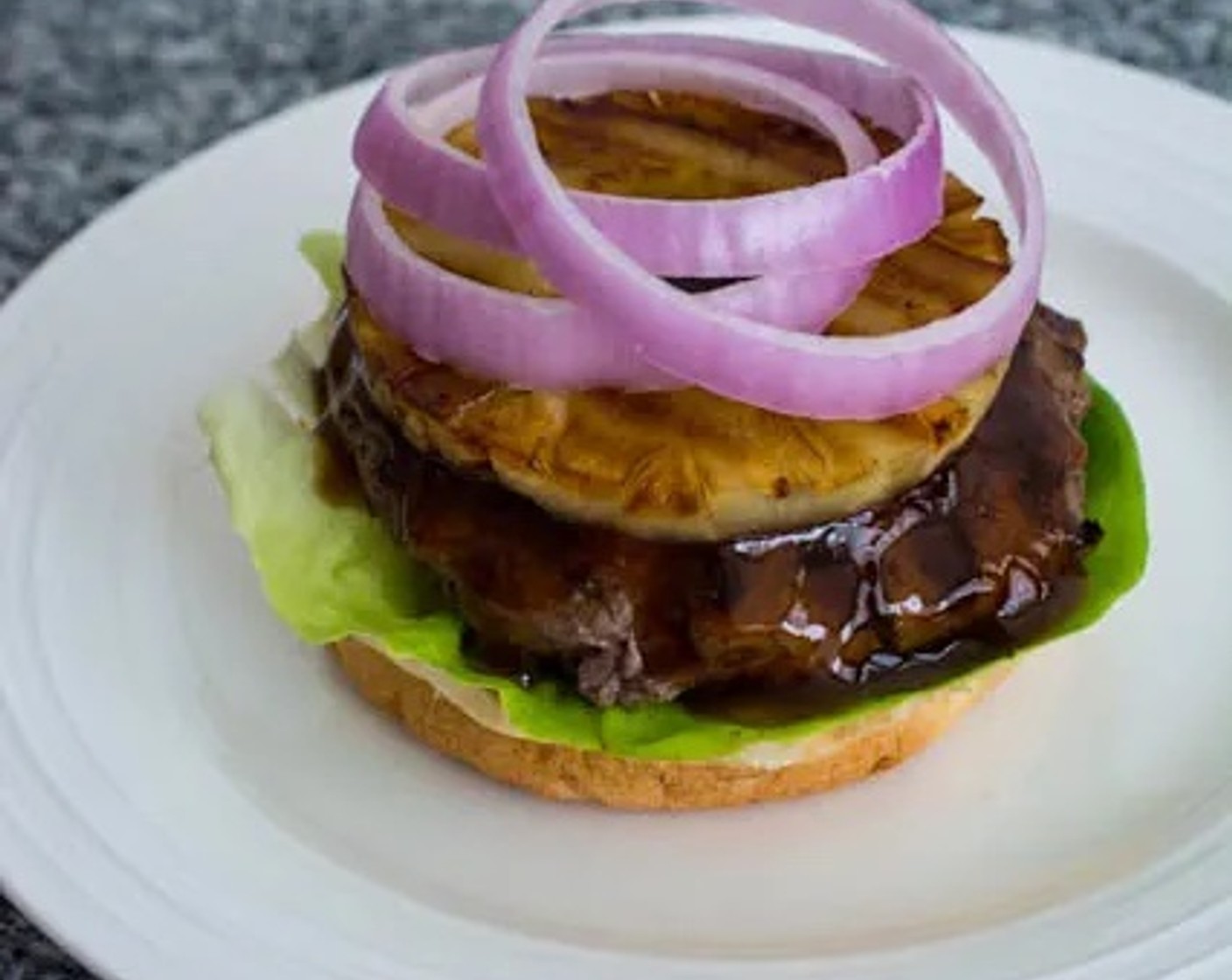 step 7 Top with a grilled pineapple ring, Onion Slices (as needed), and finally the top burger bun.