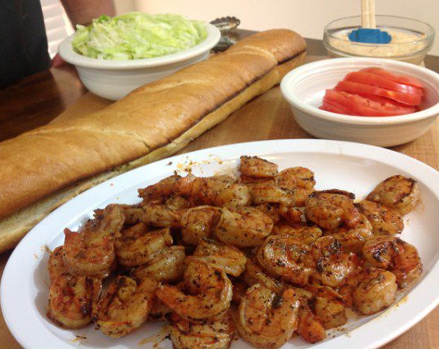 step 7 Lay the French bread on a large cutting board and layer Lettuce (to taste) and Tomatoes (to taste) on the bottom half. Pile the shrimp on top. It’s ok if a few fall off the sides