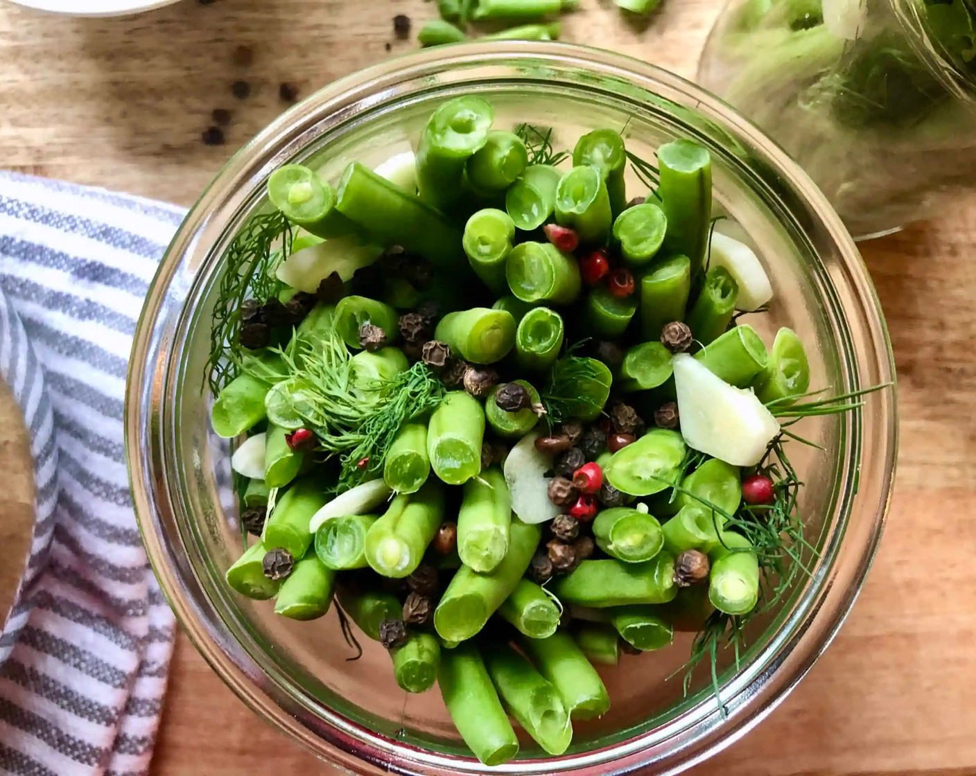 step 3 Meanwhile, fill several clean glass jars with Green Beans (4 cups) layered with pieces of Fresh Dill (8 sprigs). It is helpful to start off by laying the empty jar on its side as you place the beans within. When almost full, stand the jar upright and insert more beans wherever you notice a gap. Scatter the Black Peppercorns (2 Tbsp) evenly between the jars.