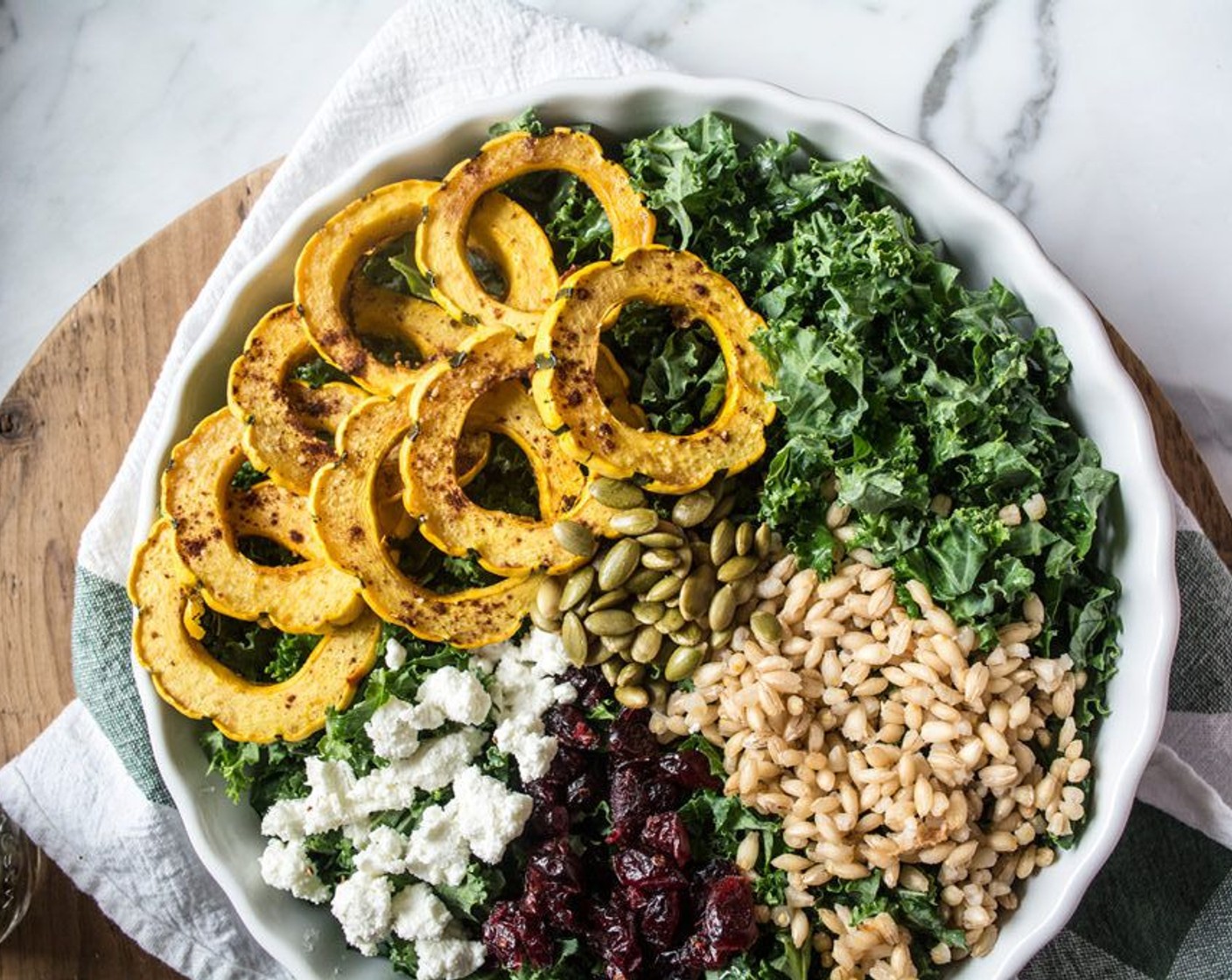 step 7 To assemble the salad, divide Kale (5 cups) between two large bowls or plates, then top each with roasted delicata squash, barley, Goat Cheese (3 Tbsp), Dried Cranberries (1/4 cup) and Pepitas (2 Tbsp).