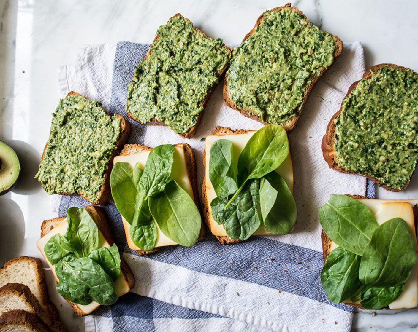 step 4 To assemble the sandwiches, lather one side of Bread (8 slices) with spinach pesto, some Fresh Baby Spinach (to taste), Goat Cheese (to taste), Caramelized Onions (to taste), and Muenster Cheese (4 slices), then top with another piece of bread. Repeat to create the other three sandwiches.