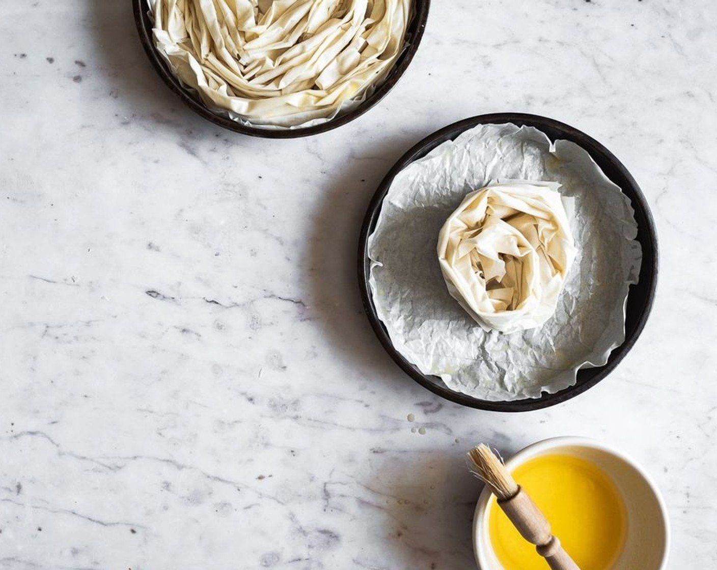 step 9 Wind up the dough into a loose, ruffled spiral, place it in your prepared pan. Repeat this process with the rest of the phyllo dough, placing each additional ruffled set of phyllo around the initial spiral to create a large rosette (you should need about 7-8 sets of ruffled phyllo to loosely fill the pan)