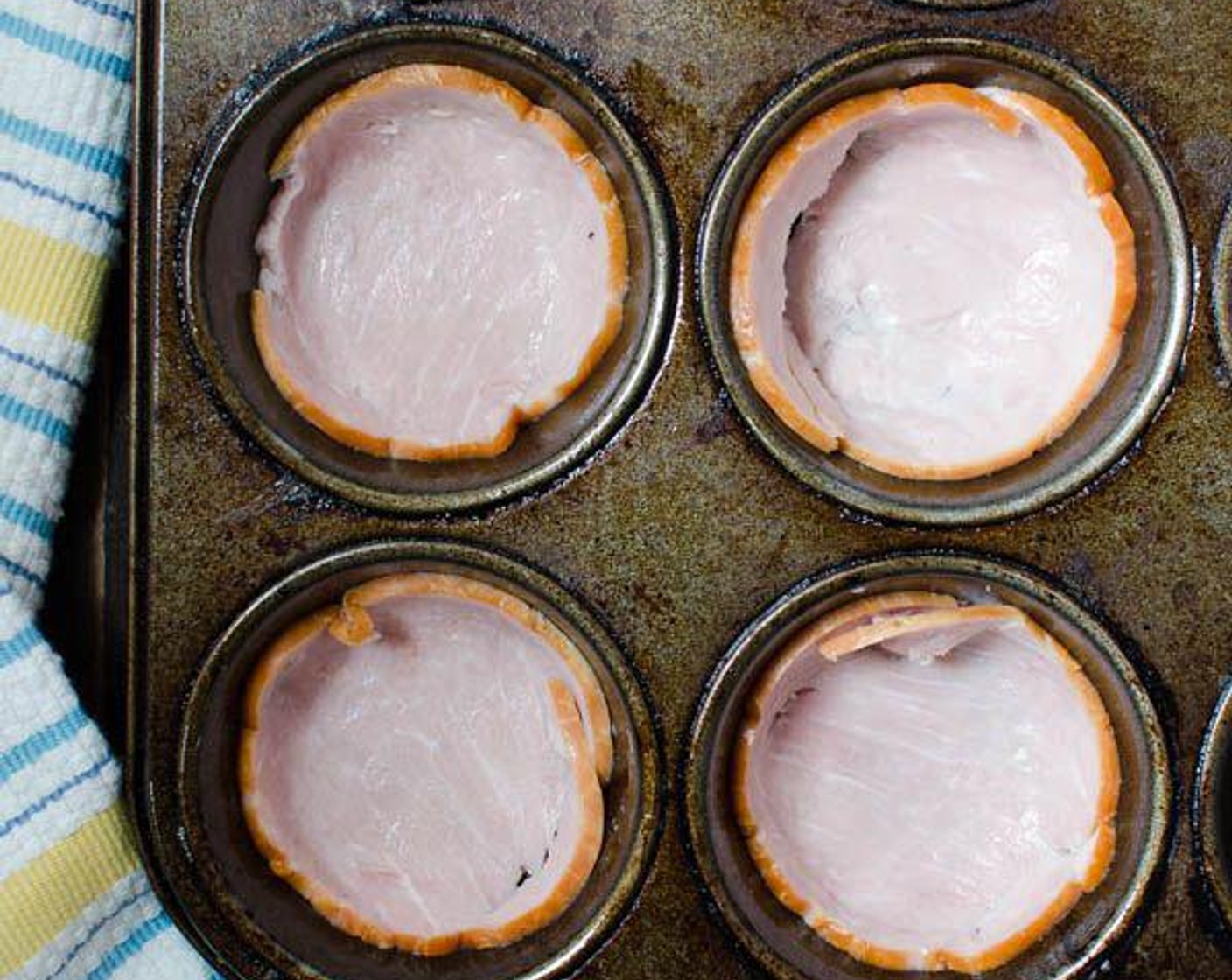 step 4 Place a slice of Canadian Bacon (4 slices) in each of the prepared tins and press it into the muffin form.
