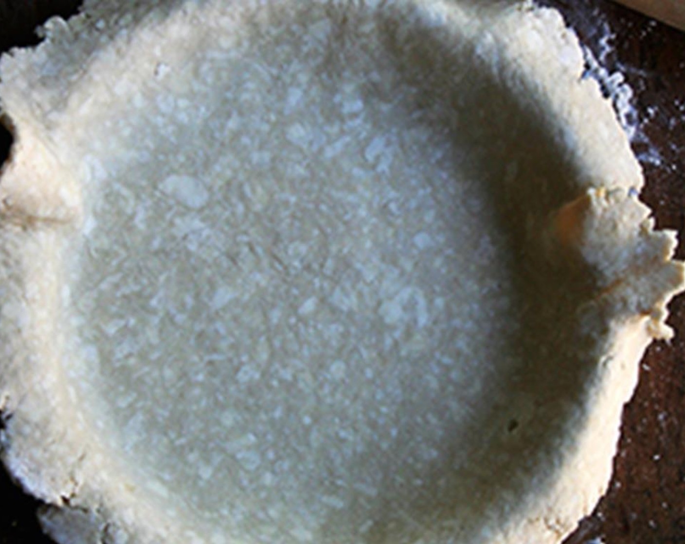 step 7 On a lightly floured work surface, place one pie dough round in the center. Roll out into a circle two inches larger in diameter than your pie plate. Fold into quarter. Place in your pie plate and unfold. Press down gently so that the dough fits into the corners.