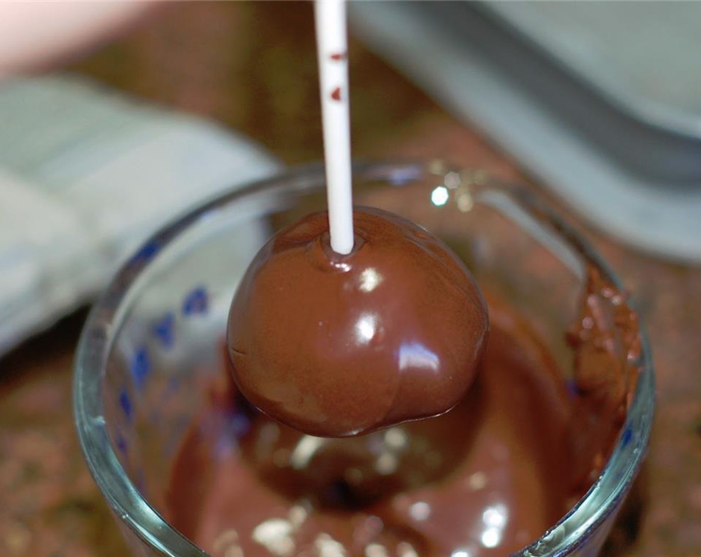 step 6 When the candy melt has hardened, pick up by the stick and dip the Oreo balls into candy coating until all covered. Once covered, remove and softly tap and rotate until excess candy melt falls off.