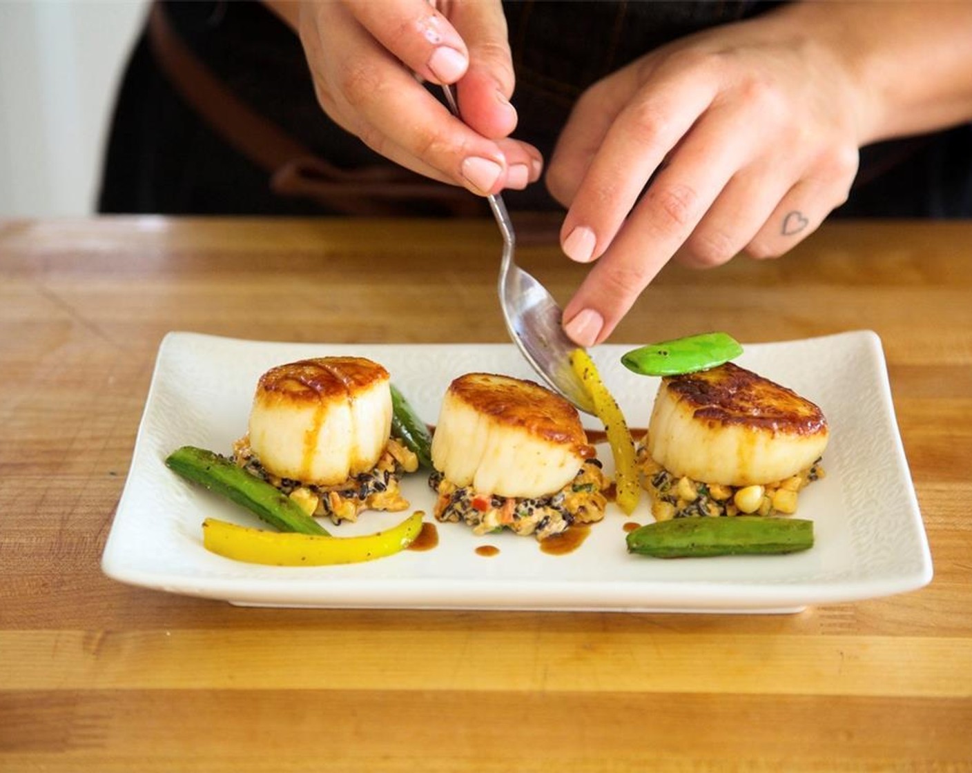 step 17 Place three small scoops of rice on two plates. Lay three scallops on top of the rice and drizzle sauce over and around the dish on each serving. Place yellow bell pepper, snap peas, and cherry tomatoes around the plate. Garnish with green onions.