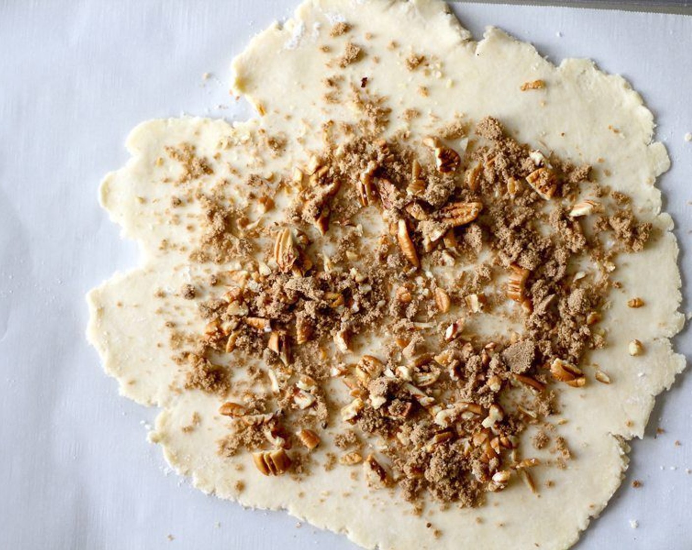 step 8 Transfer the dough circle to parchment-lined baking sheet. Sprinkle dough with the Pecans (1/4 cup) and Brown Sugar (2 Tbsp), leaving 1/2 inch bare.