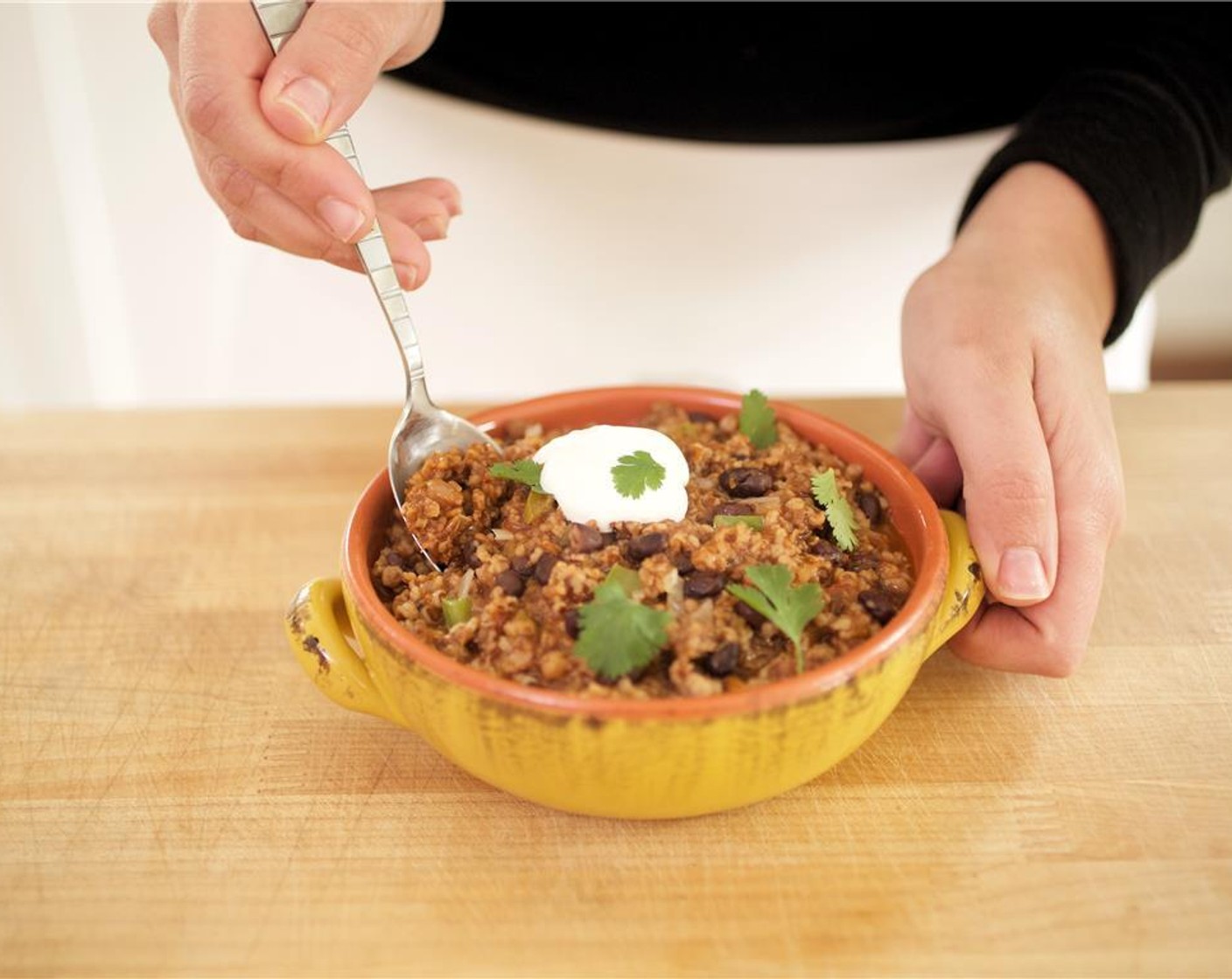 step 8 Divide the chili between two bowls. Garnish each bowl with sour cream in the center. Top with cilantro sprigs and serve with lim wedges.