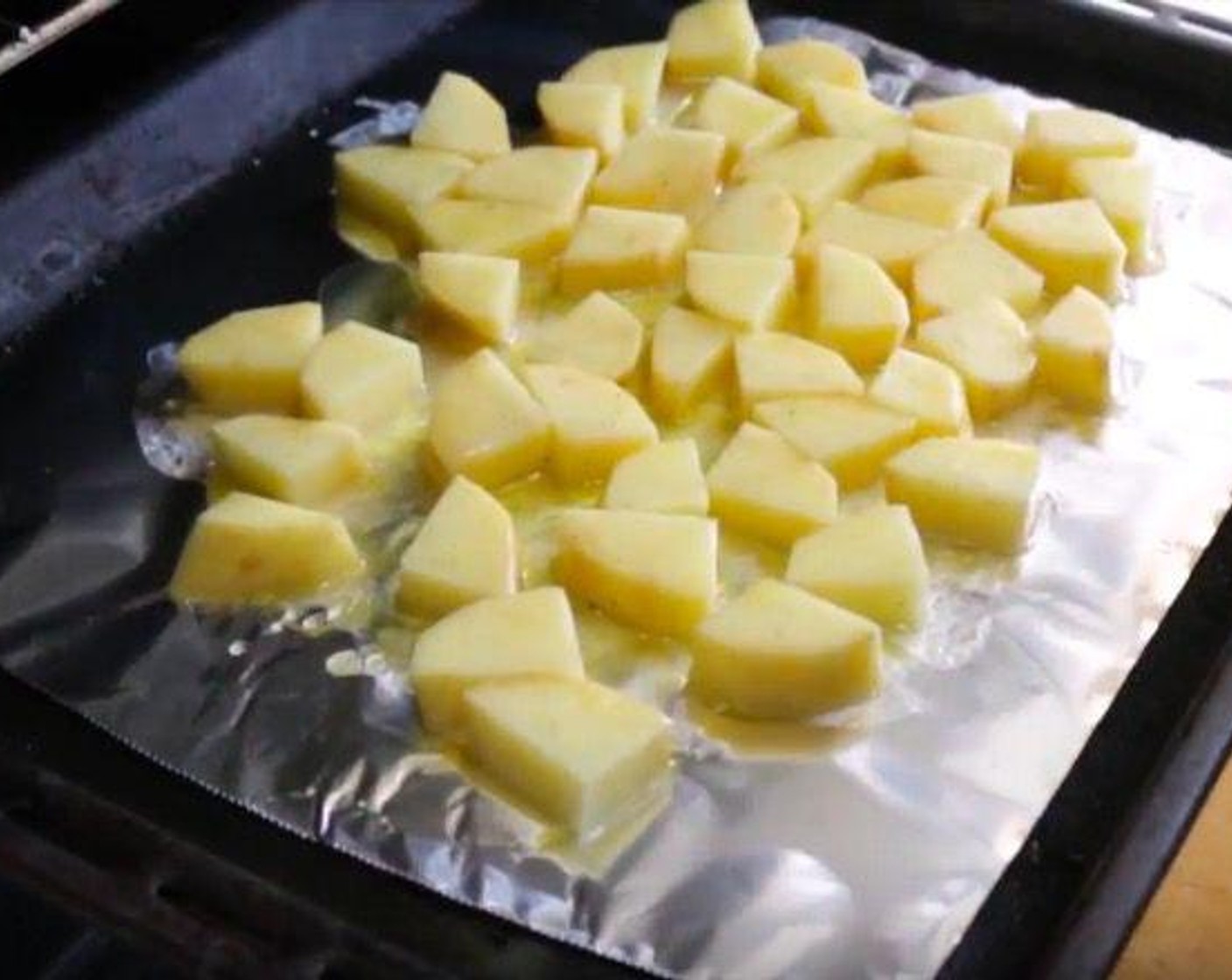 step 5 Peel and cut each of the Yukon Gold Potatoes (2) into 4 quarters and cut each quarter into 6 evenly sized pieces. Transfer into a large bowl, then drizzle with Extra Virgin Spanish Olive Oil (1 Tbsp) and season with Sea Salt (to taste) and Cracked Black Pepper (to taste). Toss together until well combined. Transfer the potatoes onto a baking tray lined with foil paper, making sure the potatoes are all in a single layer.