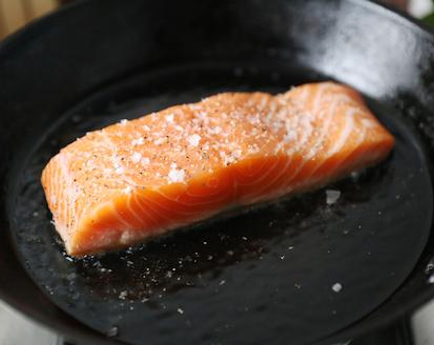 step 3 Immediately after adding the oil, lay the skin-side of the salmon fillet down away from you. Season the top with Kosher Salt (1 pinch) and Freshly Ground Black Pepper (1 pinch). Cook for 3 to 4 minutes.