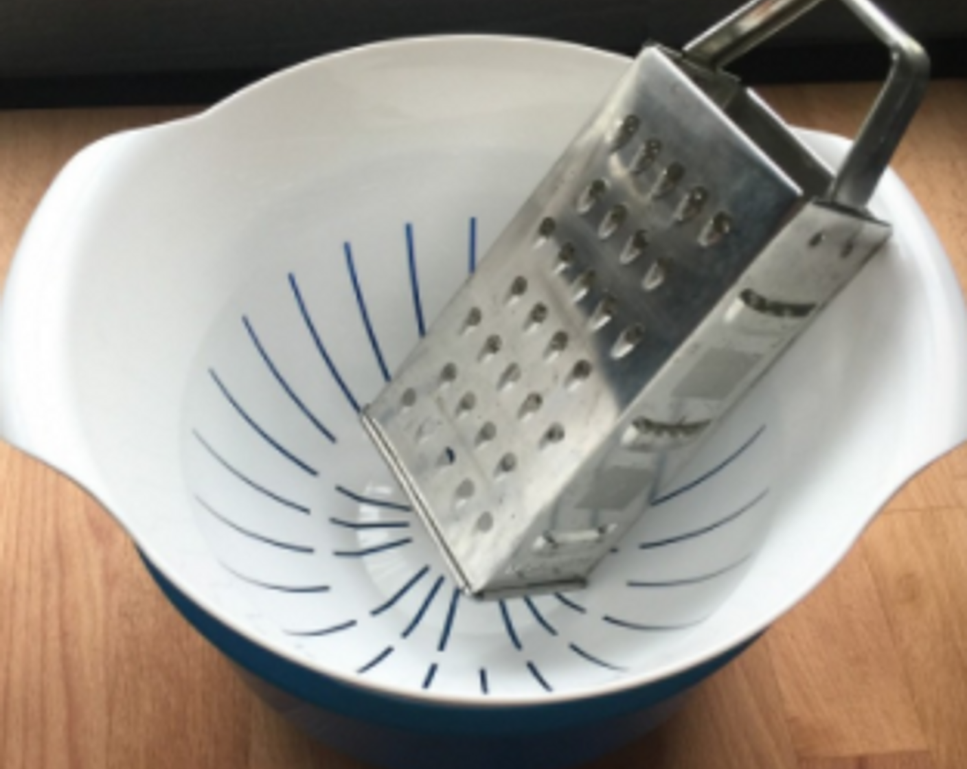 step 9 To hand-grate the pineapples, place a strainer over a large plastic or ceramic bowl and place a grater in it.