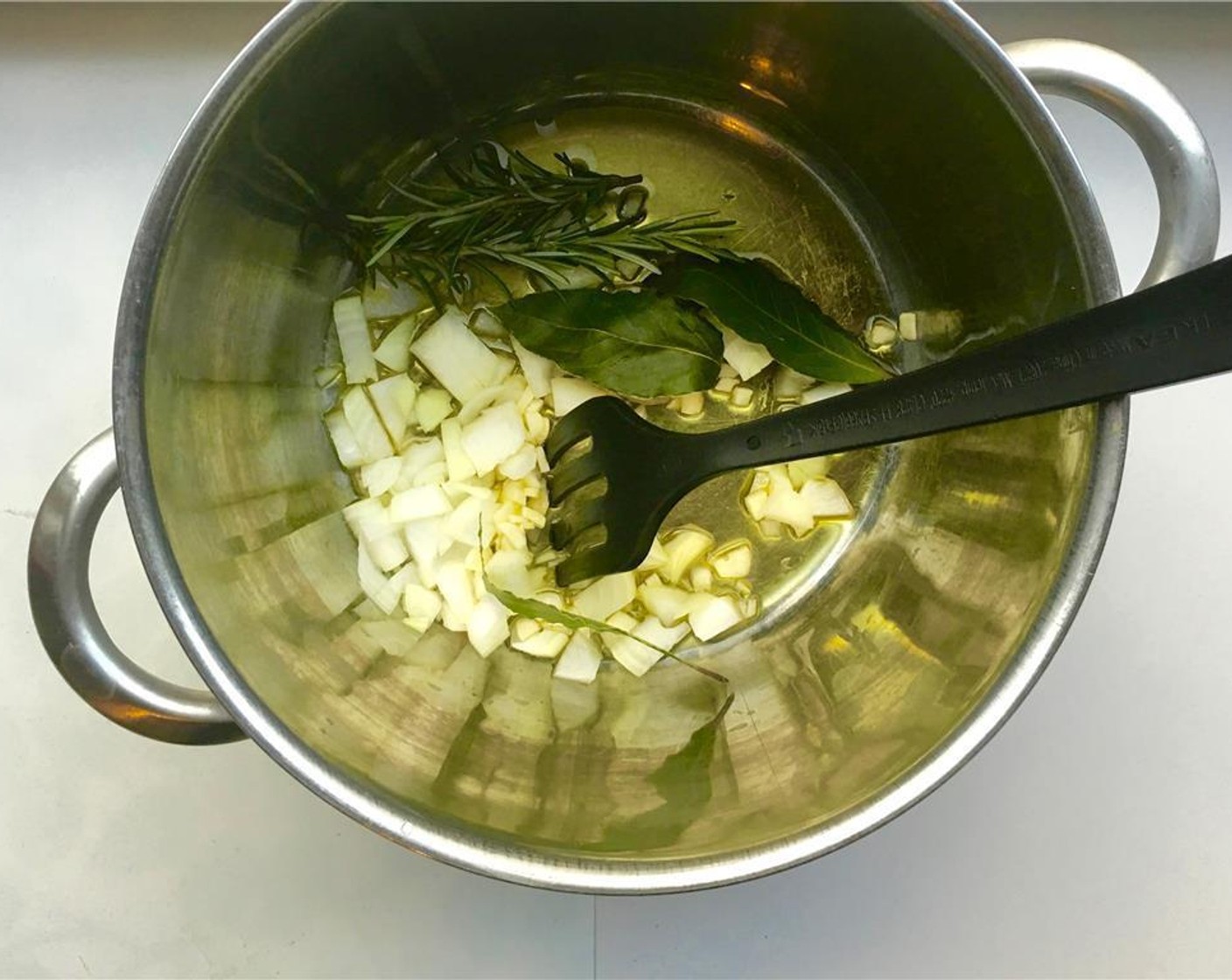 step 2 In a high pan, pour a good splash of Olive Oil (as needed) and place it over medium heat. Once hot, add the Yellow Onion (1), Garlic (5 cloves), Fresh Rosemary (2 sprigs), and Bay Leaves (3). Stir and cook for about 5 minutes.