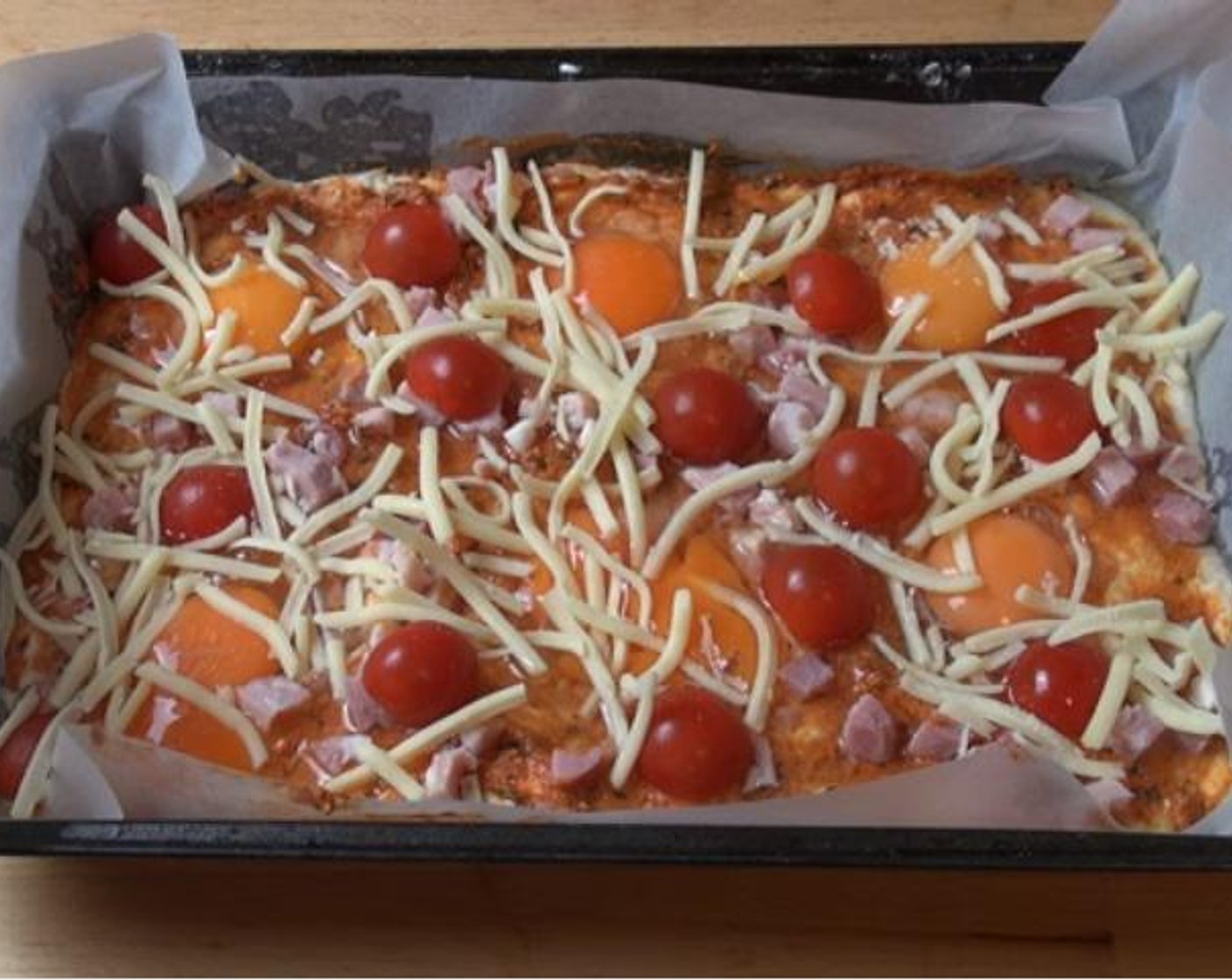 step 3 Line a baking tray with baking paper, and press the dough inside until it reaches all the corners. Top the surface with Basil Pesto (2 Tbsp), Bacon (4.5 oz), Eggs (6), halved Cherry Tomatoes (to taste) and Cheese (1/2 cup).