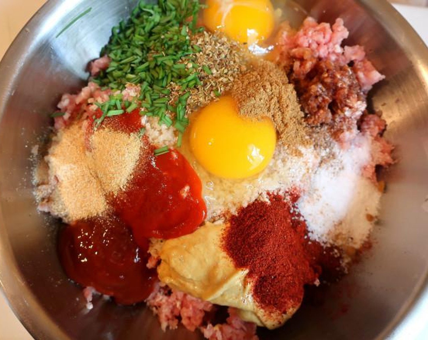 step 1 Mix Ground Pork (2 lb), Eggland's Best Classic Eggs (2), Granulated Garlic (1 tsp), Smoked Paprika (1 tsp), Ground Cumin (1 tsp), Sriracha (1 Tbsp), Ketchup (1 Tbsp), Dijon Mustard (1 Tbsp), Dried Oregano (1 Tbsp), Fresh Cilantro (1 Tbsp), Fresh Chives (1 Tbsp) and Panko Breadcrumbs (1/2 cup). Mix well but don’t overwork or the texture will become too dense.