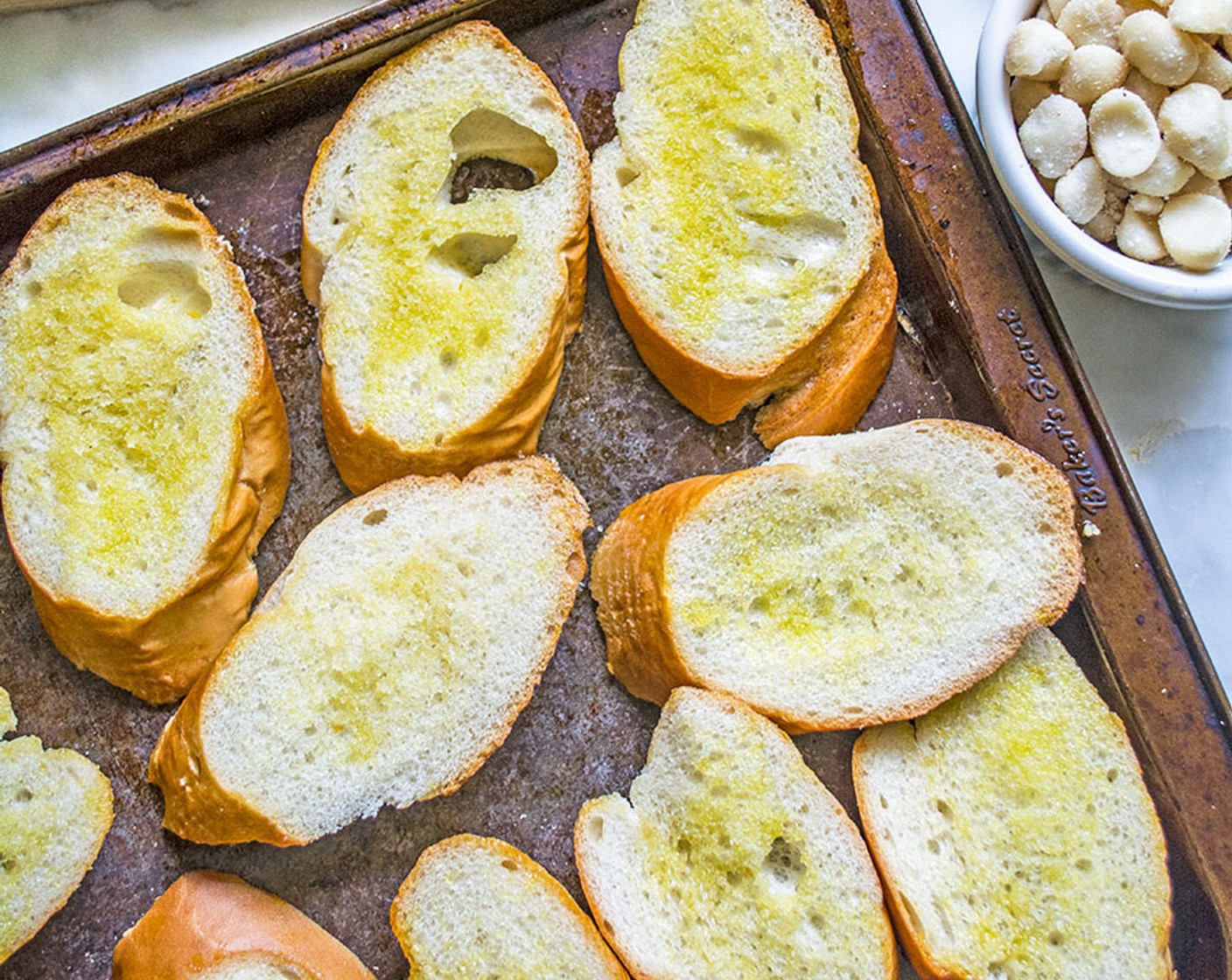 step 2 Add Olive Oil (4 Tbsp) to a small bowl. Then dip silicone brush into the oil and brush both sides of each slice of Baguette (1 loaf). Place the slices on a large baking sheet and bake for 10 minutes, flipping halfway through.