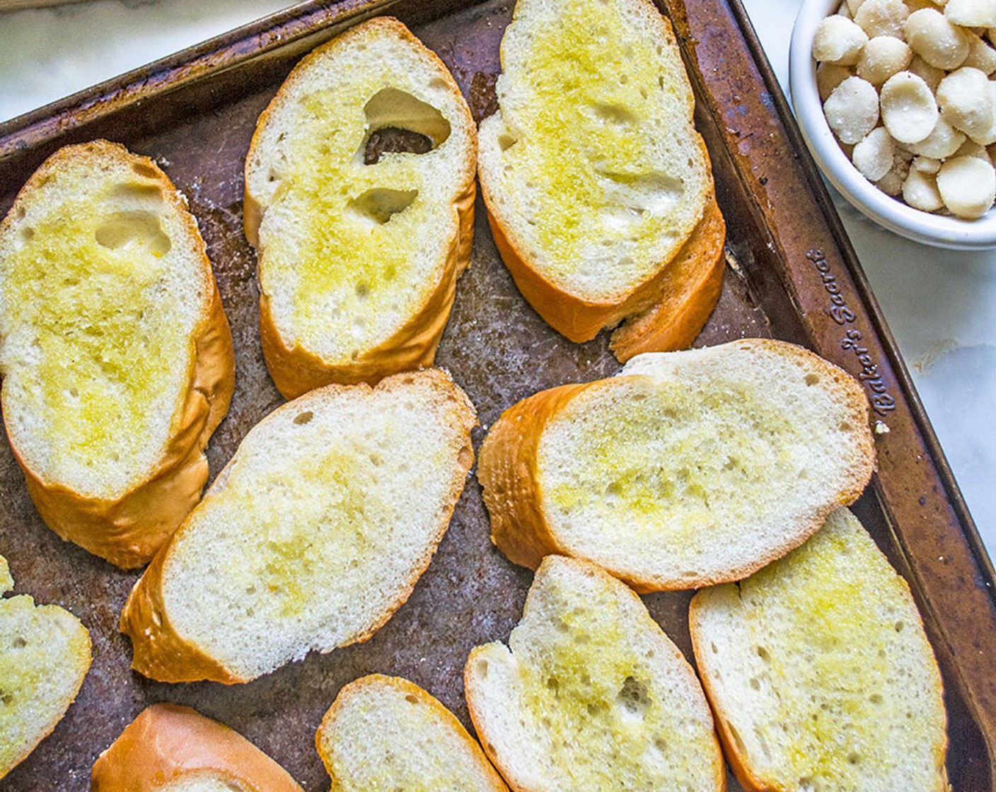 step 2 Add Olive Oil (1/4 cup) to a small bowl. Then dip silicone brush into the oil and brush both sides of each slice of Baguette (1 loaf). Place the slices on a large baking sheet and bake for 10 minutes, flipping halfway through.