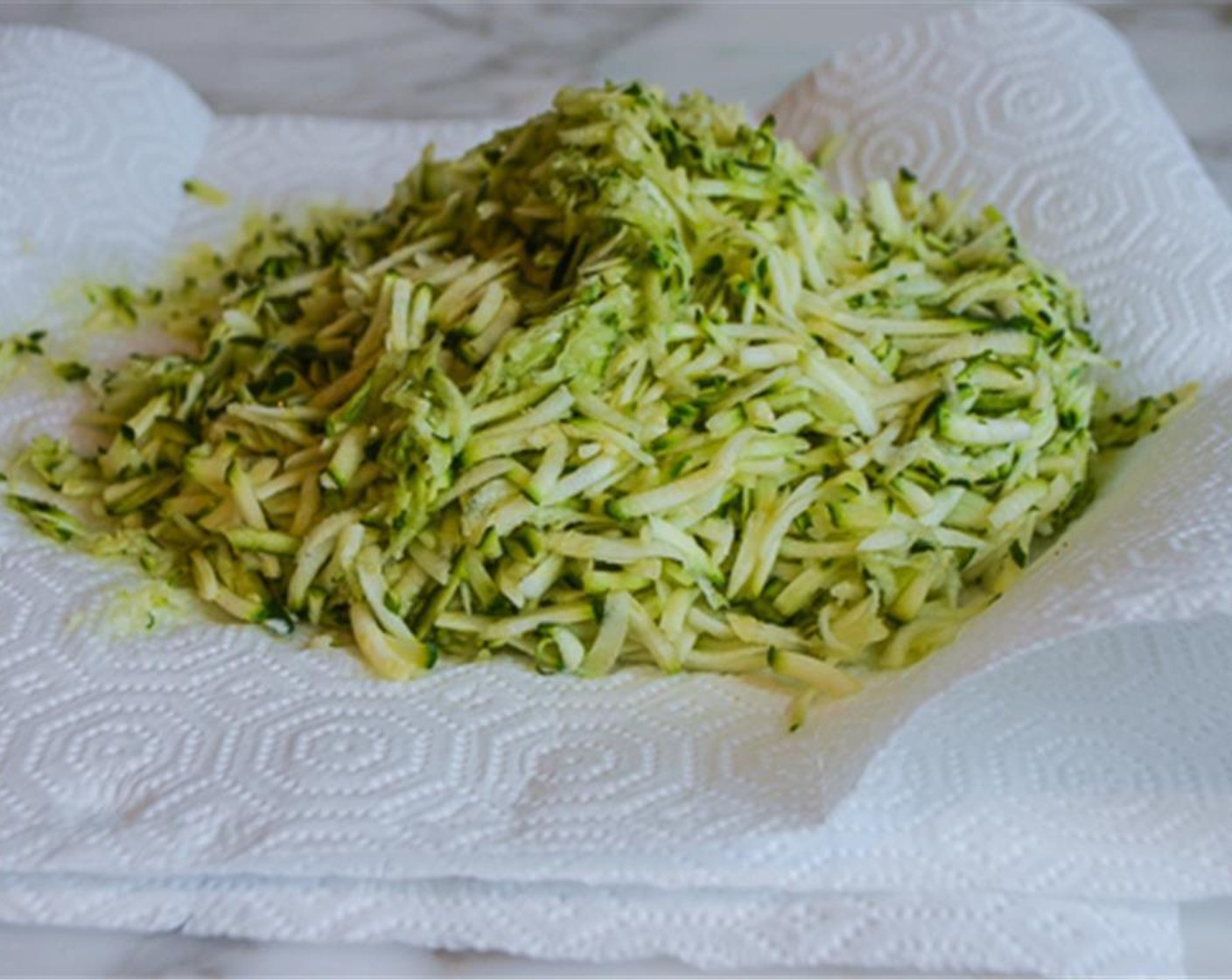 step 2 Using a food processor or box grater, grate the Zucchini (2 3/4 cups). Place the grated zucchini on top of several layers of paper towels and wring dry. If necessary, repeat 1 to 2 times to remove any excess moisture.