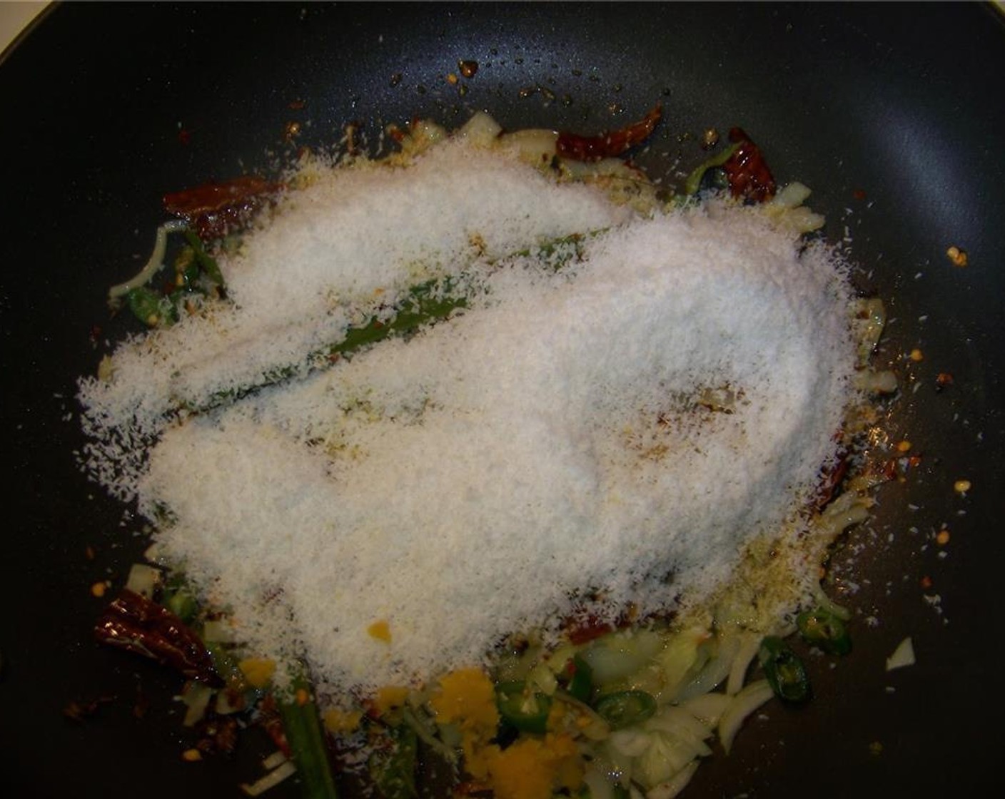 step 3 In a pan, heat canola oil. Add the remaining Onion (1/2), Curry Leaves (10), Pandan Leaves (1), Dried Chili Peppers (3), Mustard Seeds (1 Tbsp), and Green Chili Peppers (2). Once the onion begin to soften, add the Desiccated Coconut (1 cup), Salt (to taste) and Red Chili Powder (1 tsp).