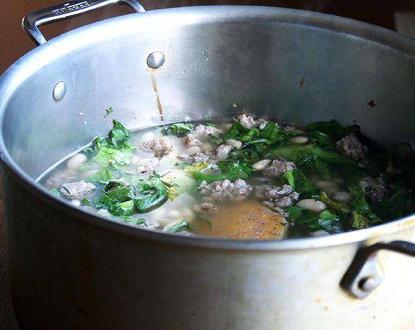 step 6 Add a half pound of the escarole to the pot. Pat it down with a wooden spoon so that it’s submerged. Once it has wilted, add the sausage. Stir. If the soup looks like it needs more beans and greens, add them; if you like your soup on the brothier side, let it be.