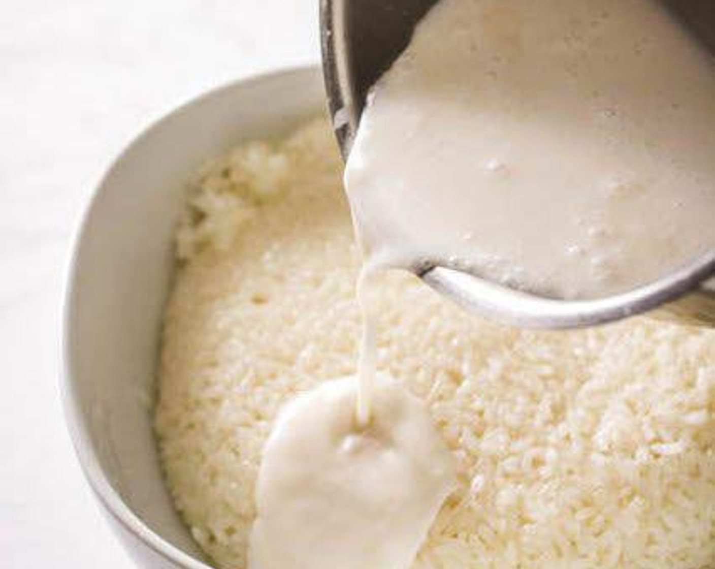 step 4 Put the steamed glutinous rice into a large mixing bowl. Pour the remaining coconut milk over the rice. Stir the coconut milk into the rice until evenly distributed.