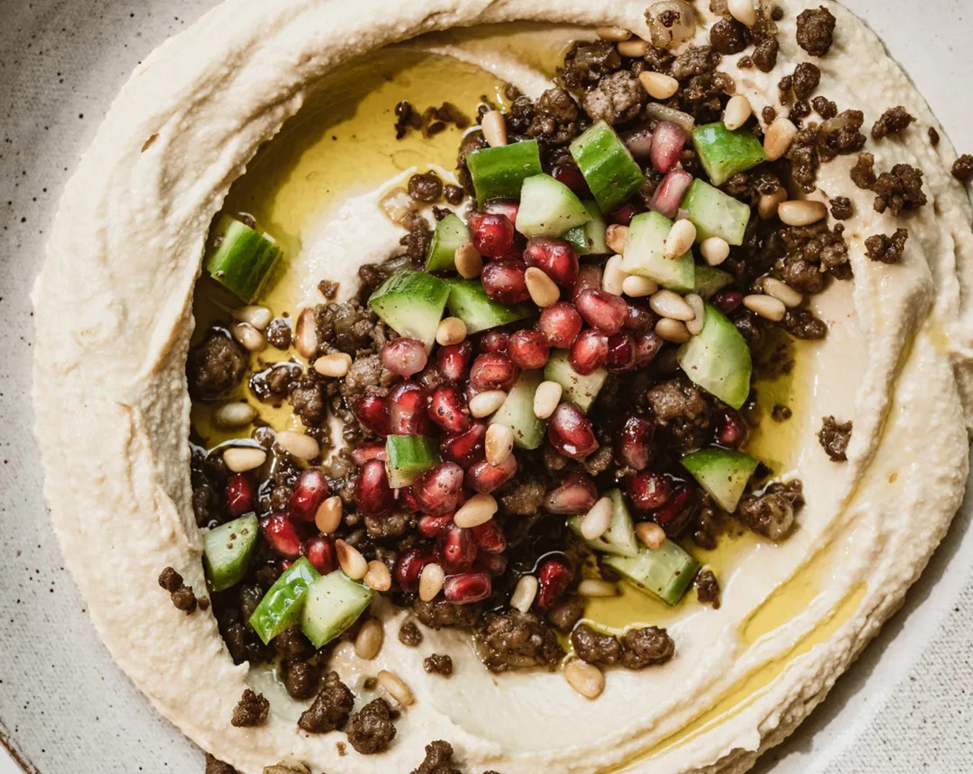 step 8 Divide hummus between two plates. Smooth hummus around the serving plate with a spoon while creating a well in the center. Drizzle with olive oil, top with spiced meat, and toasted pine nuts. Garnish with a sprinkle of Fresh Parsley (to taste). Serve with warm crispy pita bread.