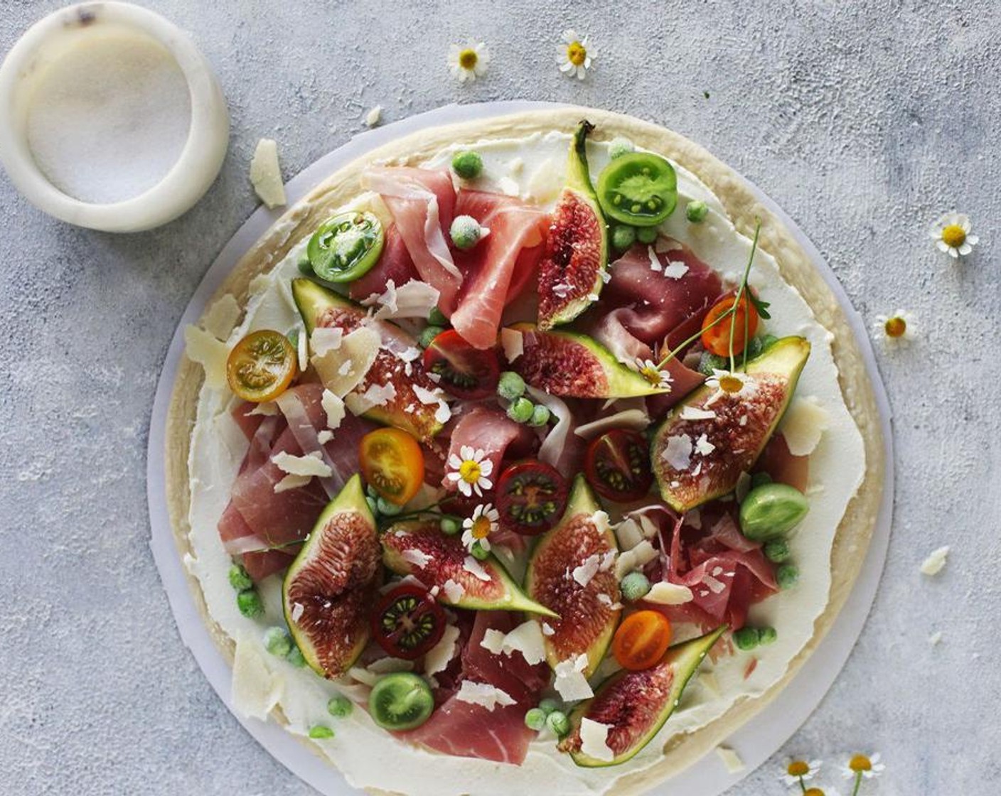 step 8 Spread the mixture on the dough, then arrange the Figs (2), Prosciutto (5 slices), Cherry Tomatoes (5), Frozen Green Peas (1/4 cup), and Parmigiano-Reggiano (1/4 cup) over the top.