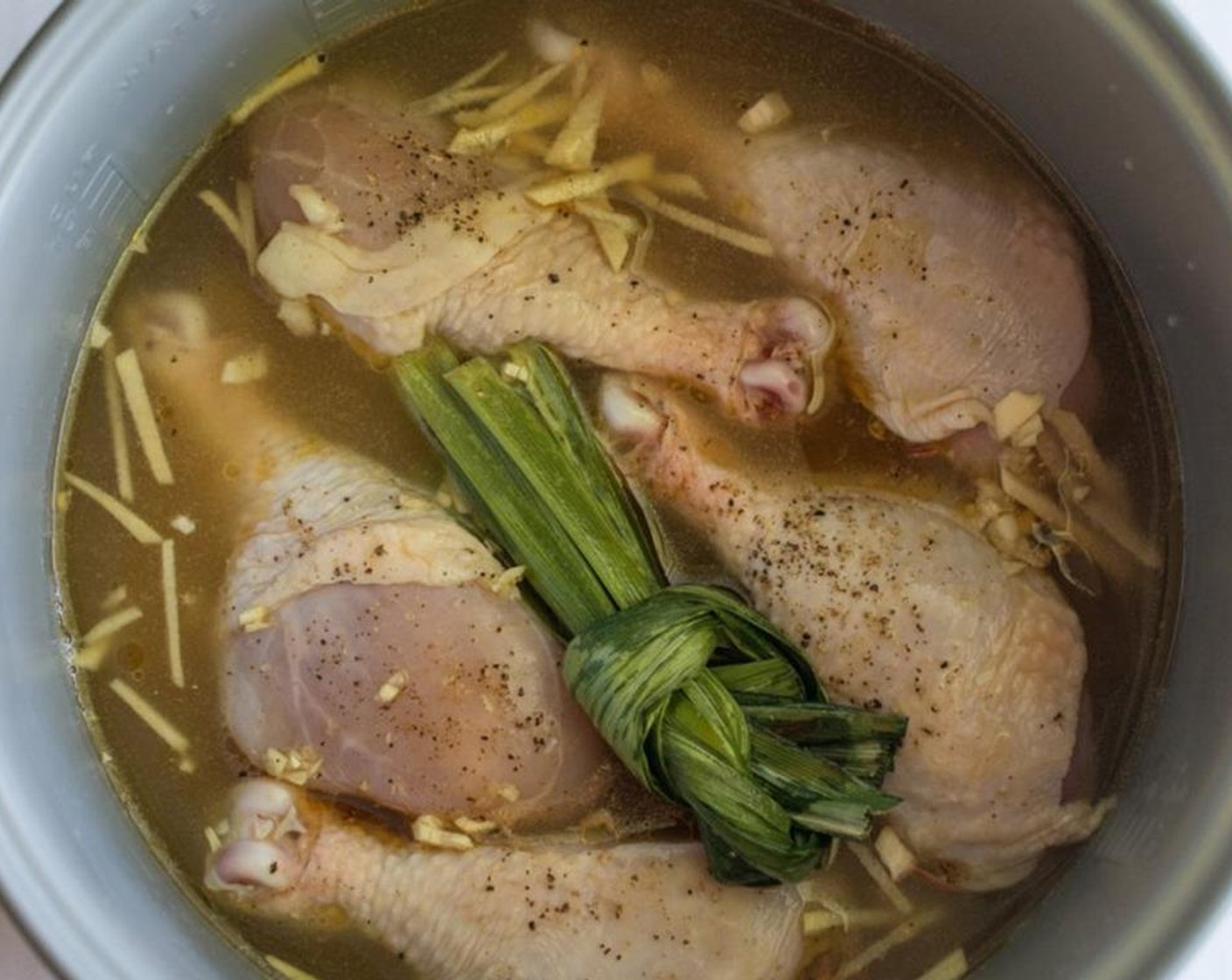 step 2 After washing and draining the White Rice (2 cups) put it into the rice cooker. Add the Chicken Stock (3 cups), Fresh Ginger (1 in), Garlic (3 cloves), and Pandan Leaves (3). Arrange the chicken drumsticks over the rice. Turn on the rice cooker and let it cook.