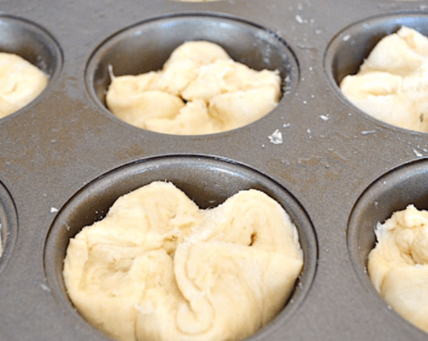 step 11 Put a square of dough into each well. Bring the corners of the square into the center so that each of the kouign amann look like little four leaf clovers. Sprinkle the tops generously with more granulated sugar. Put the tin aside to rise for another 30 minutes.