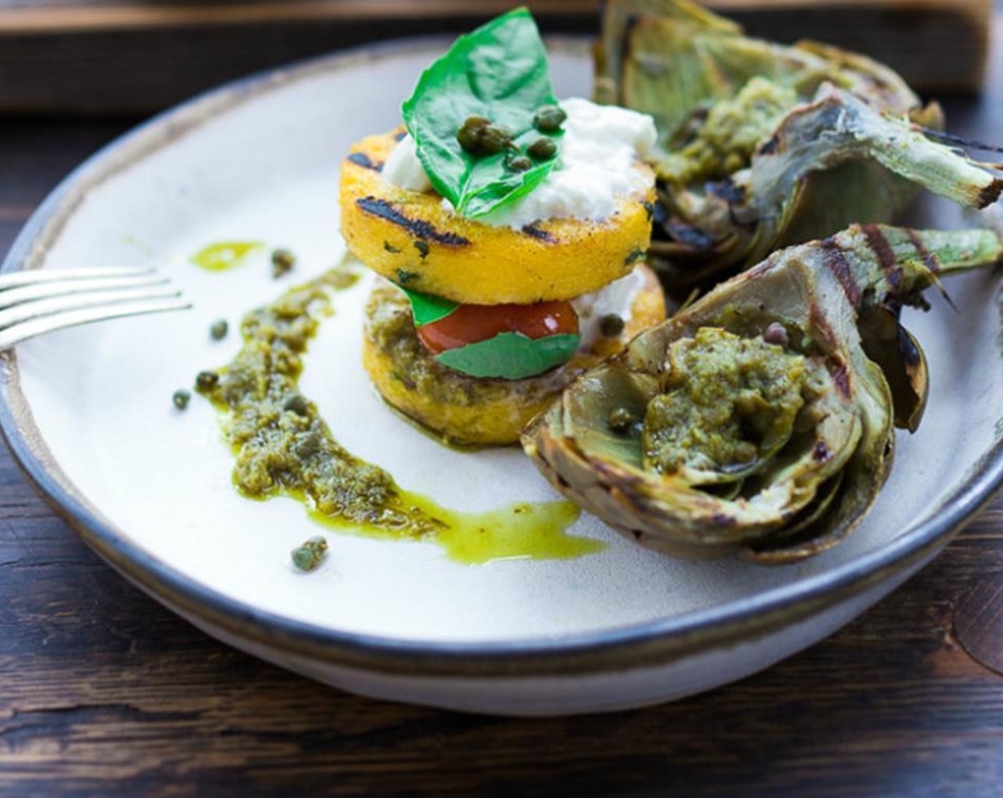 step 17 This can also be individually plated. Layer polenta, burrata cheese, pesto, tomatoes, basil and top with polenta. Surround with pesto and capers and a couple grilled artichoke wedges. Enjoy!